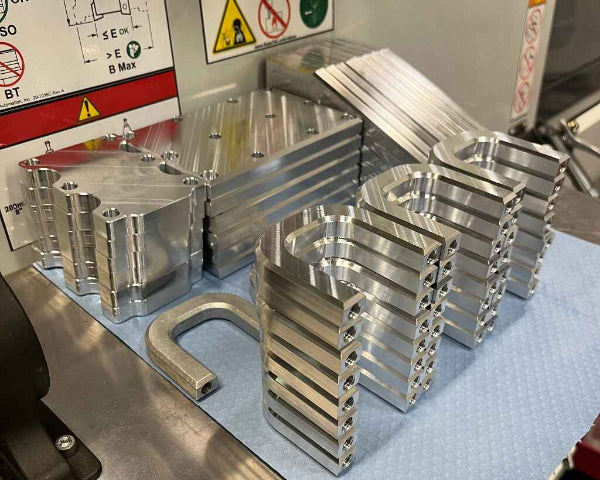 Stack of metal components on a workbench with safety signs in the background